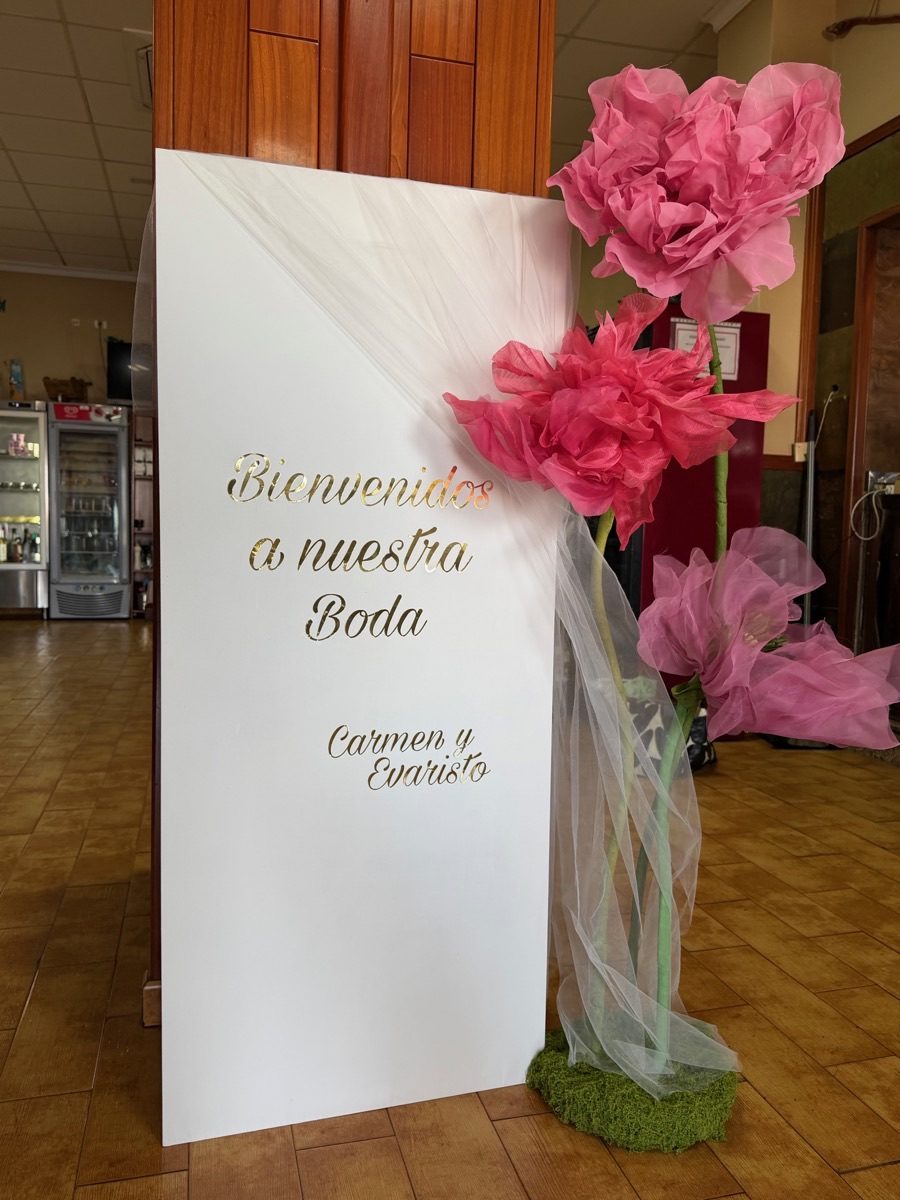 Ejemplo de cartel de bienvenida personalizado para boda con letras doradas y flores gigantes rosas, de Krealindo